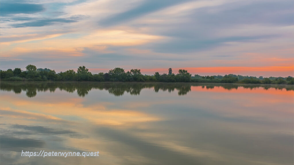 Photo by Peter Wynne of sunrise over a lake with orange, yellow, blue reflections.