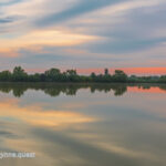 Photo by Peter Wynne of sunrise over a lake with orange, yellow, blue reflections.