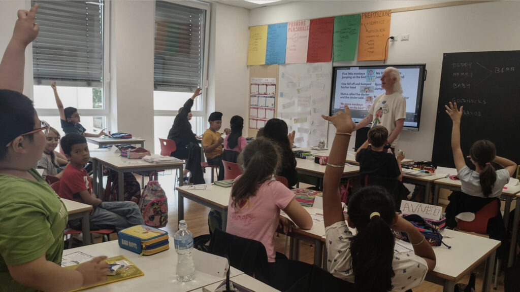 Photo of Peter in a classroom of young children with their hands up wanting to respond to a question.